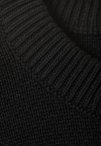 Gros plan sur un tissu en maille noire montrant des motifs en côtes et des points jersey, avec une surface douce et texturée.