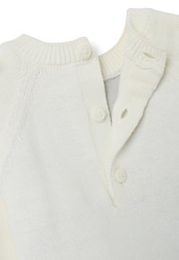 Roomkleurige gebreide trui met een geribbelde kraag, voorzien van twee knoopsluitingen en een zachte textuur, met een eenvoudig, klassiek ontwerp.