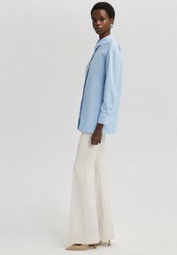 Camisa de botonadura azul claro con cuello tradicional y mangas largas, combinada con pantalones de pierna ancha crema y tacones de punta nude.