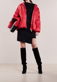 Rød foret jakke med lynlåslukning foran, båret over en sort kjole. Sorte knæhøje støvler fuldender outfittet, sammen med en sort håndtaske.