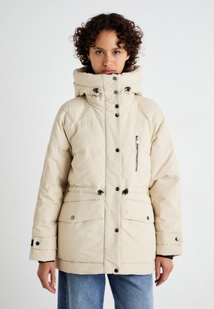Veste matelassée beige avec un col haut, cordons de serrage, poche zippée à l'avant et boutons-pression. Dispose d'une texture matelassée et d'une coupe décontractée.