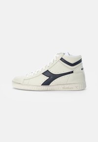 Baskets mi-hautes blanches avec des accents noirs, en cuir, avec des détails perforés et une semelle en caoutchouc texturée. Design à lacets avec logo.