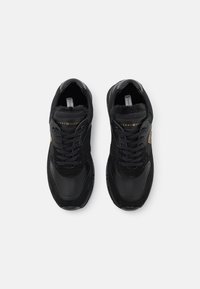 Black sneakers made of leather and suede with a textured finish. Features laces, padded collar, and gold logo accent. Flat rubber sole.