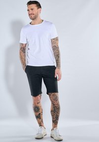 Weiße Kurzarm-T-Shirt, schwarze Shorts und weiße Sneaker. Verfügt über stilisierte Tattoos an Armen und Beinen. Sauberer, lässiger Look.