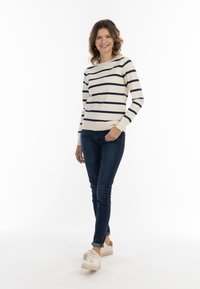 Pulover rayat în crem cu dungi bleumarin, asortat cu blugi skinny de culoare albastru închis și adidași de culoare deschisă. Design simplu, croială lejeră.