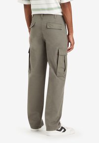 Gröna cargo-byxor med avslappnad passform, som har flera stora fickor och ett slitstarkt bomullsmaterial. Innehåller en logotypstämpel på baksidan.