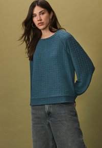 Teal textuur sweatshirt met een relaxte pasvorm, lange raglanmouwen en een ronde halslijn, gecombineerd met lichtgewassen denim jeans.