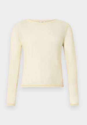 Τοπ με μακριά μανίκια σε ανοιχτό κίτρινο, κατασκευασμένο από απαλό ύφασμα. Διαθέτει στρογγυλή λαιμόκοψη και εφαρμοστή σχεδίαση με εμφανείς ραφές.