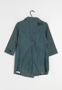 Abrigo ligero de patrón verde con cuello, mangas largas, dos botones en los puños y un detalle bordado en negro en la parte trasera.