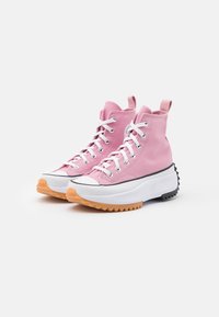 Pink high-top sneakers made of canvas with a rubber sole. Features include white laces, black and orange accents, and a textured sole.