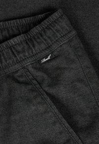 Black jogger pants made of soft fabric, featuring an elastic waistband and a small "Reell" tag stitched on the side seam.