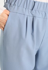 Pantalons bleu clair en tissu lisse, dotés d'un design plissé, d'une taille élastique et de poches latérales pour plus de fonctionnalité.