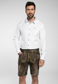Weißes Langarmhemd mit Button-Down-Kragen, kombiniert mit braunen Ledershorts, die eine dekorative Gürtelschnalle und gelbe Stickdetails aufweisen.