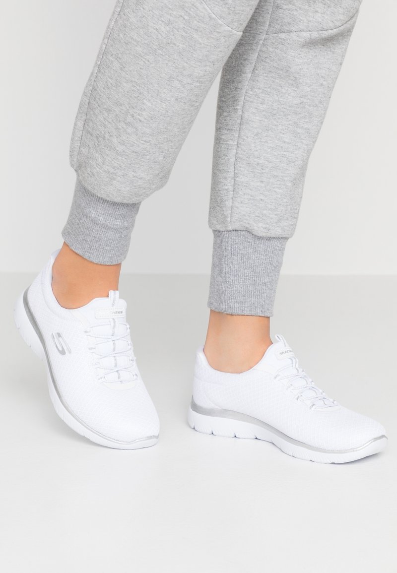 Scarpe sportive bianche con tomaia in rete, punta rotonda e un accento grigio sulla suola. Presentano lacci e logo sul lato.