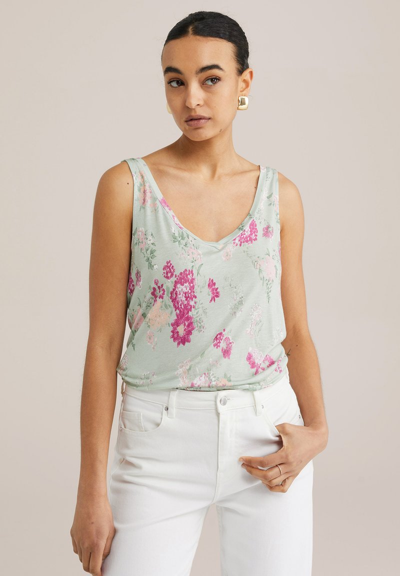 Cvečni top v svetlo zeleni barvi z rožami v rožnati in beli barvi; ima V-izrez in sproščen kroj, v kombinaciji z belimi visokimi kavbojkami.