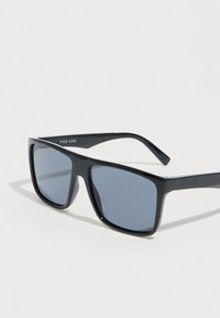 Μαύρα ορθογώνια γυαλιά ηλίου με σκουρόχρωμους φακούς και την επωνυμία "PIER ONE" στην εσωτερική πλευρά του αριστερού σκέλους.