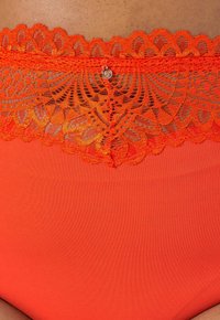 Oranje hoge tailleondergoed met een brede kantafwerking aan de bovenkant, met ingewikkelde patronen en een kleine metalen accent.