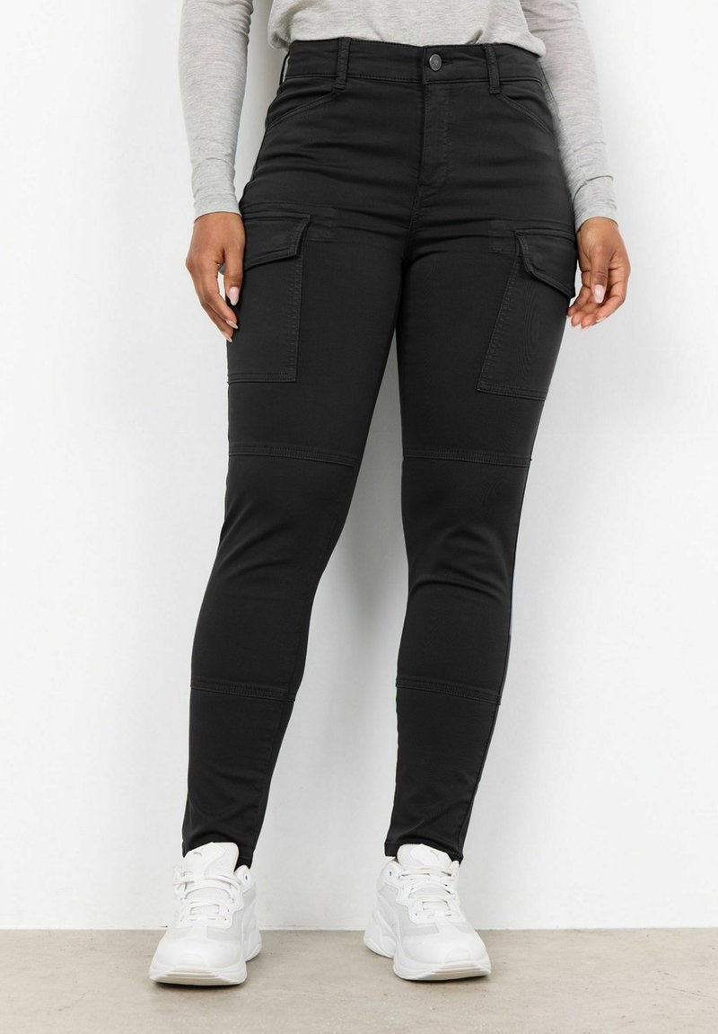 Černé vysoké cargo kalhoty s bočními kapsami, slim fit a hladkým povrchem, doplněné bílými sportovními botami.