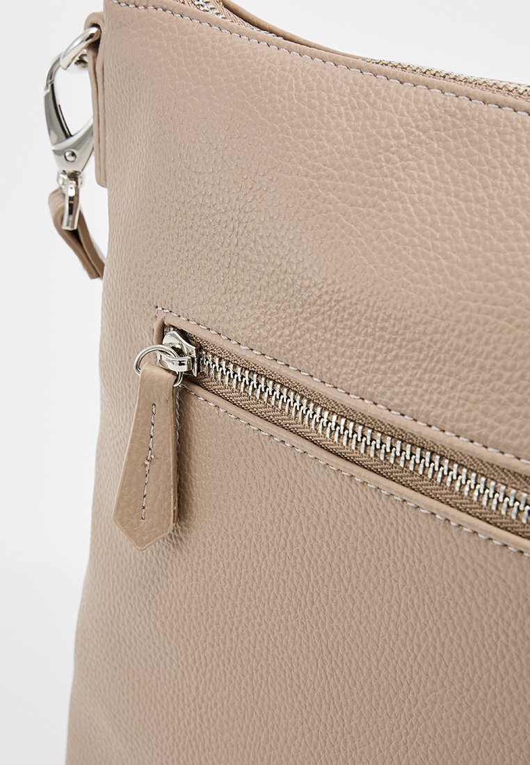 Sac à main en cuir beige avec texture granulaire, quincaillerie en argent, une poche zippée et une étiquette en cuir sur le devant pour des détails.