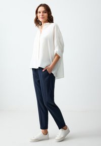 Witte overhemd met driekwartmouwen, gecombineerd met marineblauwe tapered broek en witte sneakers. Zacht materiaal, comfortabele pasvorm.
