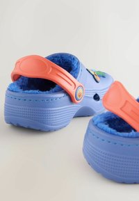 Blue rubber clogs with a plush blue interior, featuring a pink heel strap and decorative patches on the upper. Textured sole for grip.