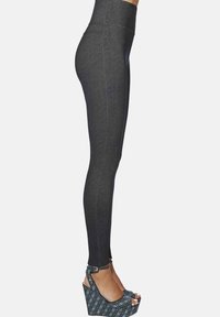 Widok z boku osoby noszącej ciemnoszare legginsy z wysokim stanem oraz wzorzyste sandały na koturnie na wysokim obcasie z paskami wokół kostek.