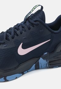 Chaussure de sport bleu foncé avec le logo Nike rose, dessus texturé, semelle noire et bleu clair à motifs, et lacets bleu marine.