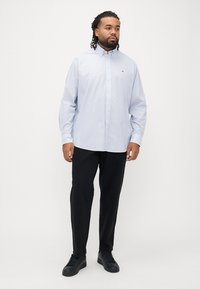 Vaaleansininen pitkähihainen kauluksellinen nappipaita, käytetty mustien housujen ja tummien tennareiden kanssa. Rintakehässä pieni logo.