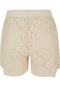 Shorts en dentelle beiges avec un motif floral, dotés d'une taille élastique et d'un ourlet légèrement arrondi sur les côtés.