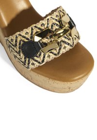 Sandale plateforme tissée beige et noire avec une semelle en liège, dotée d'une large sangle ornée d'accents dorés et noirs.