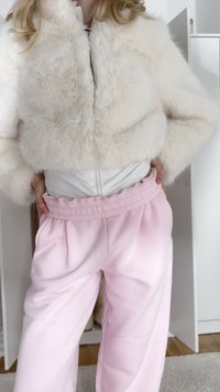 Veste courte en fausse fourrure blanche avec fermeture éclair frontale, associée à un pantalon plissé rose clair doté d'une taille élastique et d'une texture douce.
