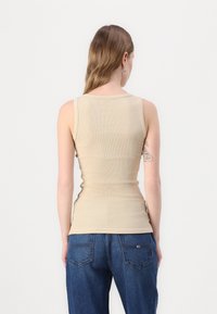 Beige ribbed tank top dengan desain yang pas dan tali bahu lebar, dipadukan dengan celana jeans denim biru high-waisted yang memiliki kantong belakang.