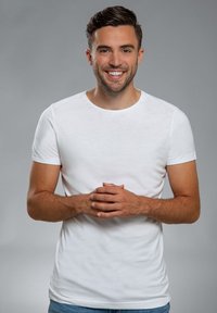 Witte korte-sleeve t-shirt met een ronde halslijn, aangesloten vorm en een gladde textuur, gedragen met blauwe spijkerbroeken tegen een grijze achtergrond.