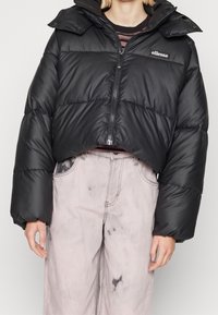 Czarna krótka pikowana kurtka z zamkiem błyskawicznym, z wysokim kołnierzem i szerokimi rękawami. W zestawie jasnoszare, postrzępione spodnie o szerokich nogawkach.