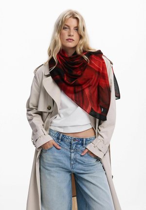 Red and black patterned scarf made of lightweight fabric, draped elegantly around the neck, contrasted against a beige trench coat and jeans.