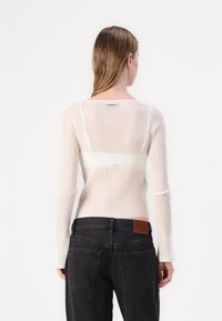 Ribbede, langermede, lys rosa genser med semi-transparent bak; har hvit horisontal stripe og etikett på baksiden av halsen.