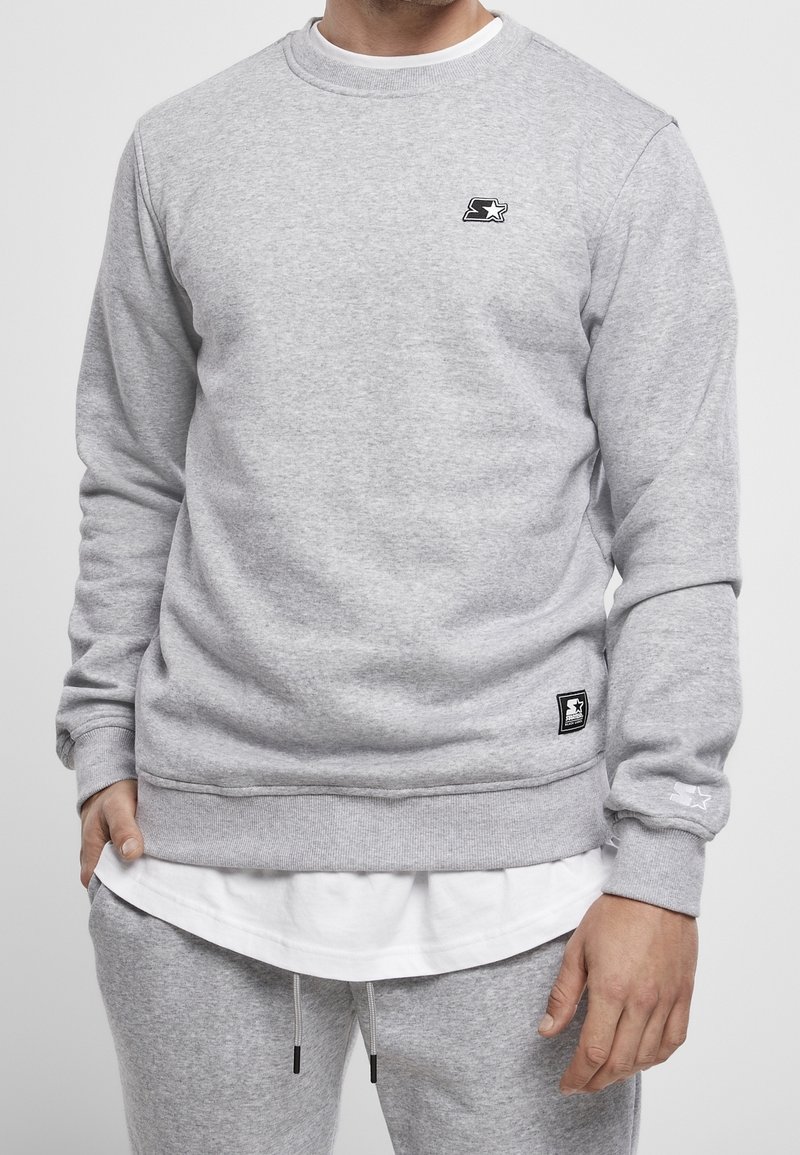 Sweatshirt en coton gris avec un col rond, des poignets et un ourlet côtelés. Présente un petit logo noir sur la poitrine et une étiquette tissée sur le côté.