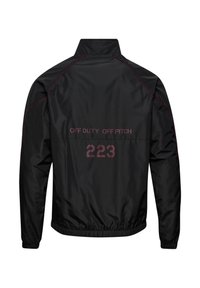 Veste légère noire avec poignets et ourlet élastiqués, passepoil rouge et texte "OFF DUTY OFF PITCH 223" dans le dos.