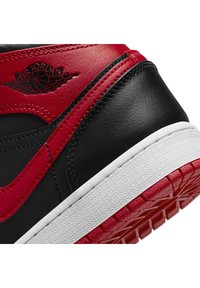 Gros plan sur un talon de basket noir et rouge avec logo Air Jordan, semelle intermédiaire blanche et semelle extérieure rouge à motif adhérent texturé.