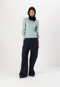 Light blue ribbed sweater with puffed shoulders, paired with loose-fitting dark denim jeans. Sweater features a black faux fur collar.