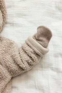 Beige teksturert stofferm med en lodden utseende, som har en lysere farget strikket mansjett og en myk, glatt bakgrunn.