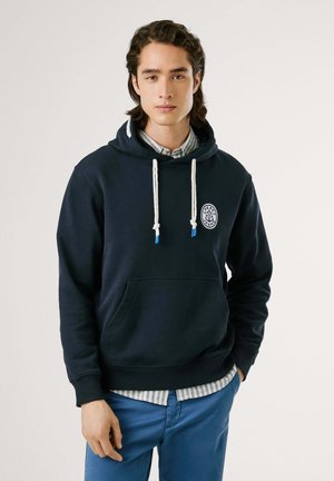 Navyblauwe hoodie van zachte stof, met een voorzak, verstelbare trekkoorden en een ronde logo-accent op de borst.