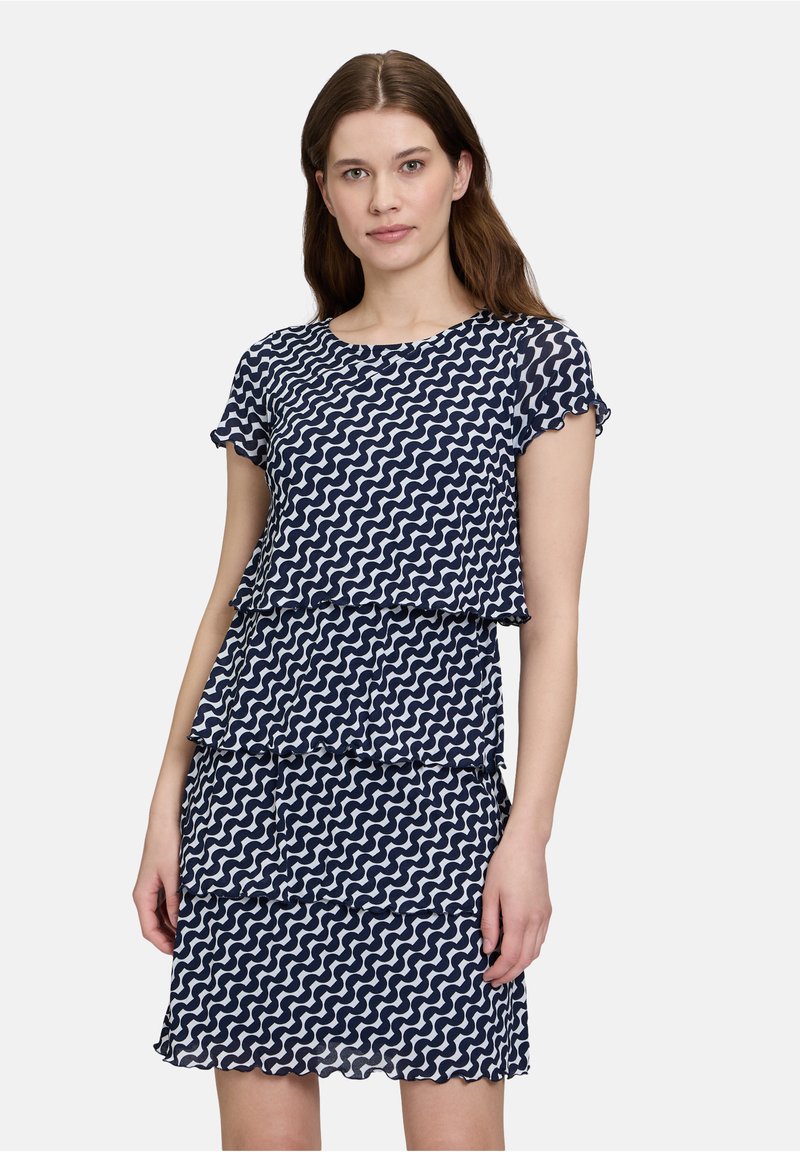 Navyblaues Kleid mit weißem wellenförmigen Muster, kurzen Ärmeln, geschichteter Gestaltung und Rüschendetails. Hergestellt aus leichtem, strukturiertem Stoff.