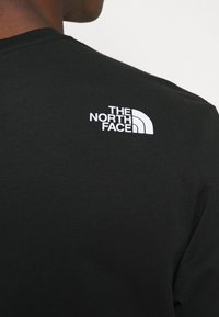 Svart bomull t-shirt med en vit logotyp av "THE NORTH FACE" på den övre delen av ryggen. Tyget ser mjukt ut med en klassisk crew neck-design.