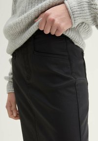 Schwarze Hosen mit einer glatten Textur, ausgestattet mit Seitentaschen und einem figurbetonten Design. Der Stoff wirkt leicht und flexibel.
