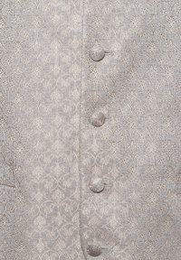 Strukturierter Stoff in hellbeige mit einem detaillierten Blumenmuster. Verfügt über fünf mit Stoff bezogene Knöpfe an der Vorderseite.