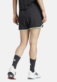 Pantalones cortos deportivos negros con ribete verde, fabricados en tela liviana, con una cintura elástica y combinados con zapatillas blancas y calcetines negros.