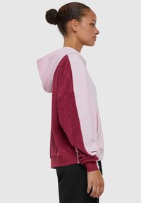 Hoodie met een bicolor ontwerp, heeft een roze lichaam en bordeauxrode mouwen. Het materiaal heeft een zachte, gestructureerde uitstraling.