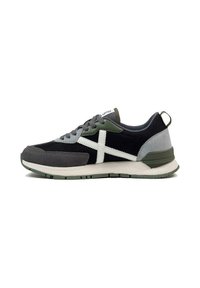 Zapatilla deportiva negra y gris con acentos blancos, que cuenta con una parte superior texturizada, detalles en verde y una suela acolchada para mayor comodidad.