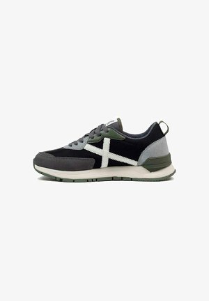 Chaussure de sport noire et grise avec des accents blancs, présentant une tige texturée, des détails verts et une semelle rembourrée pour le confort.